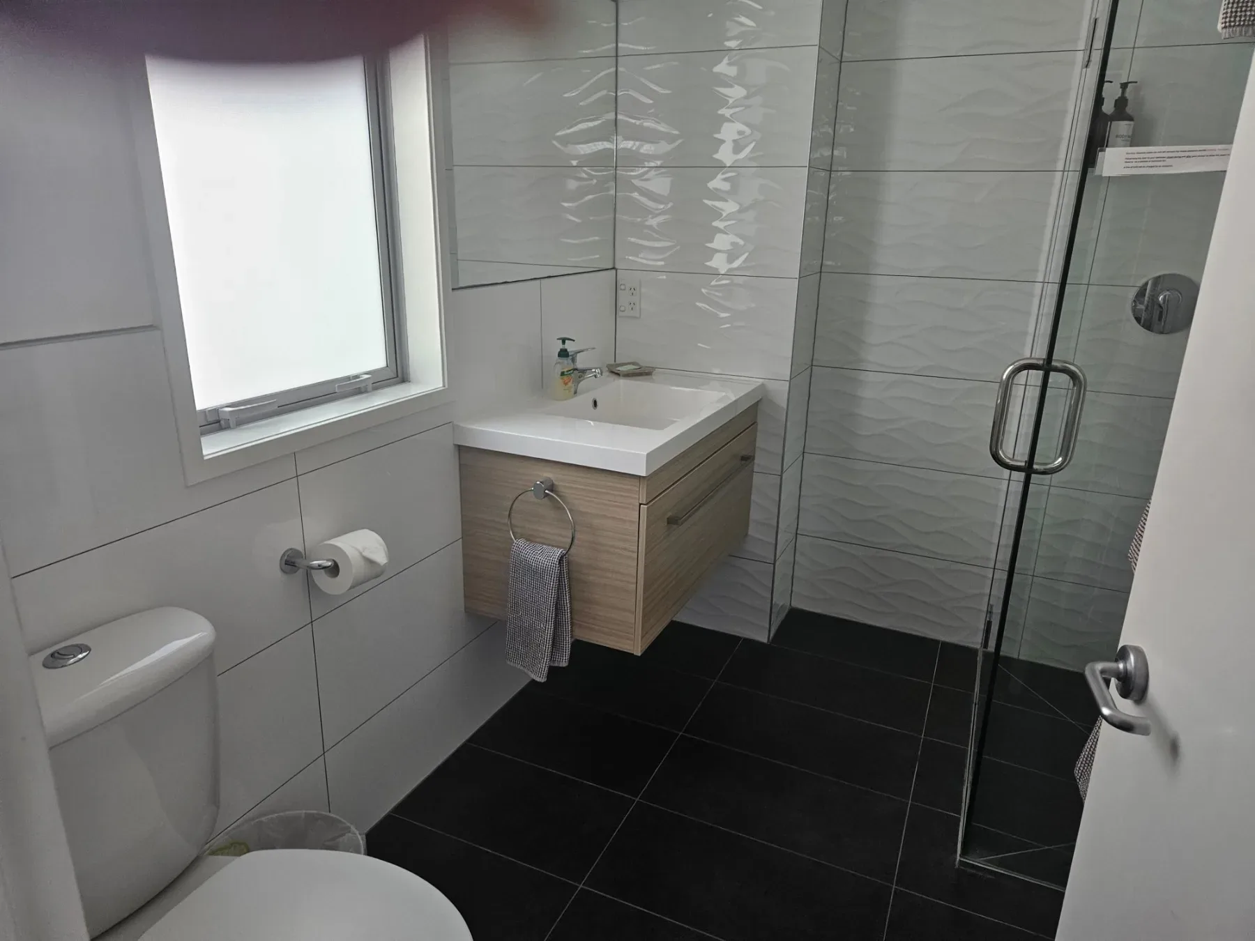 Bathroom with glass shower, vanity and dark tiled floor.