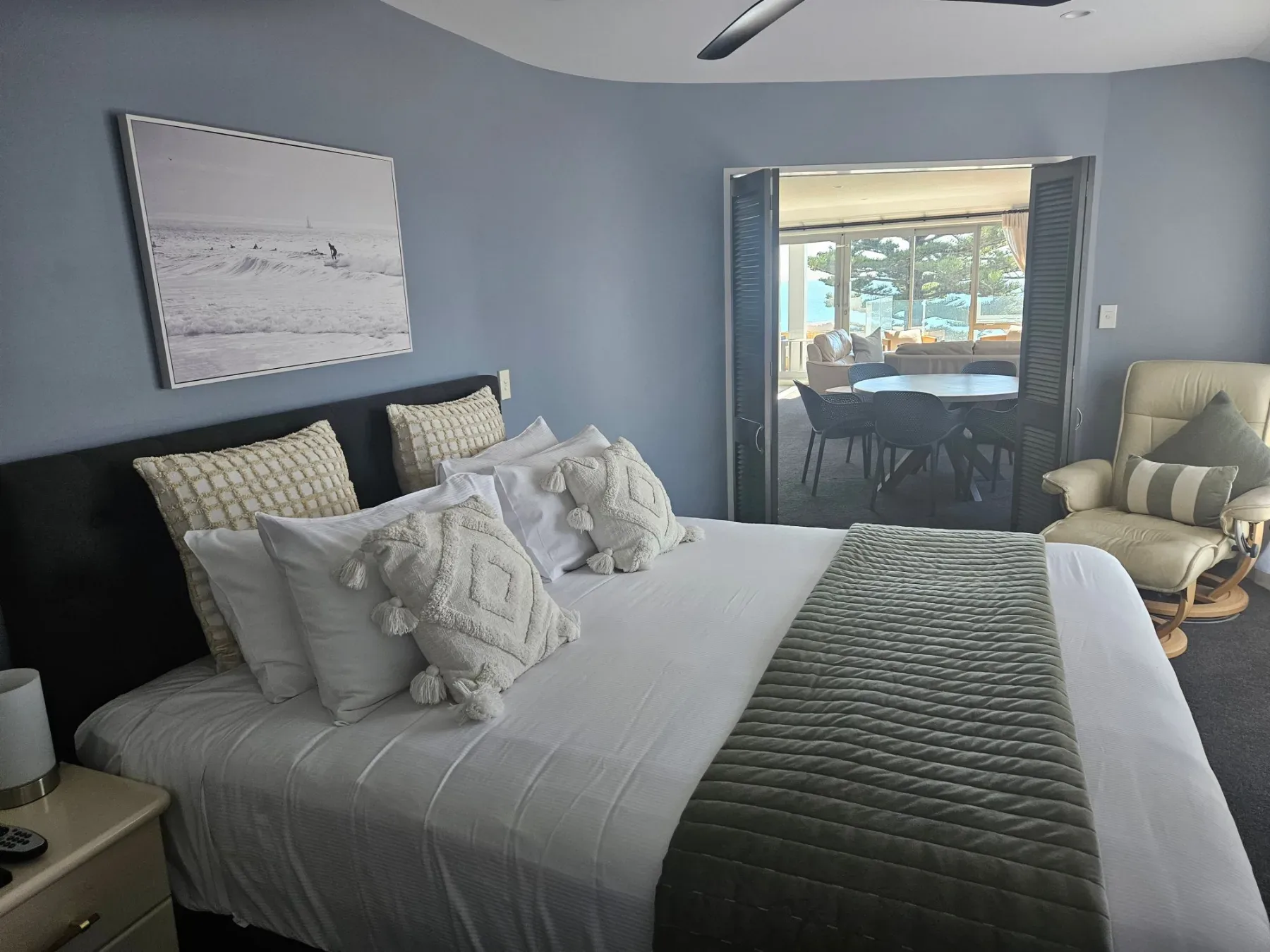 Bedroom with king bed, green throw and doorway through to the ocean-view living area.