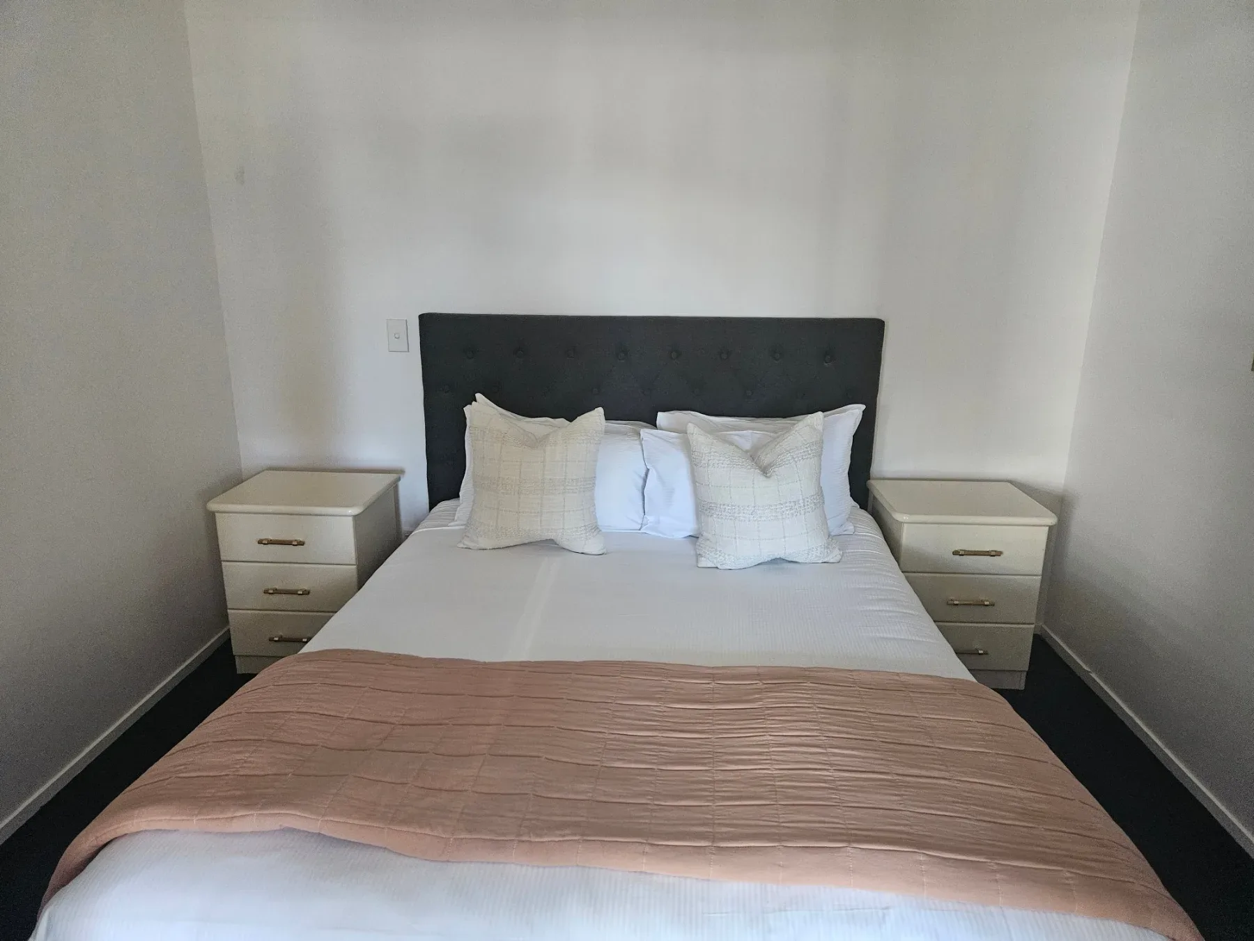 Bedroom with tufted headboard, white bedding and peach throw.