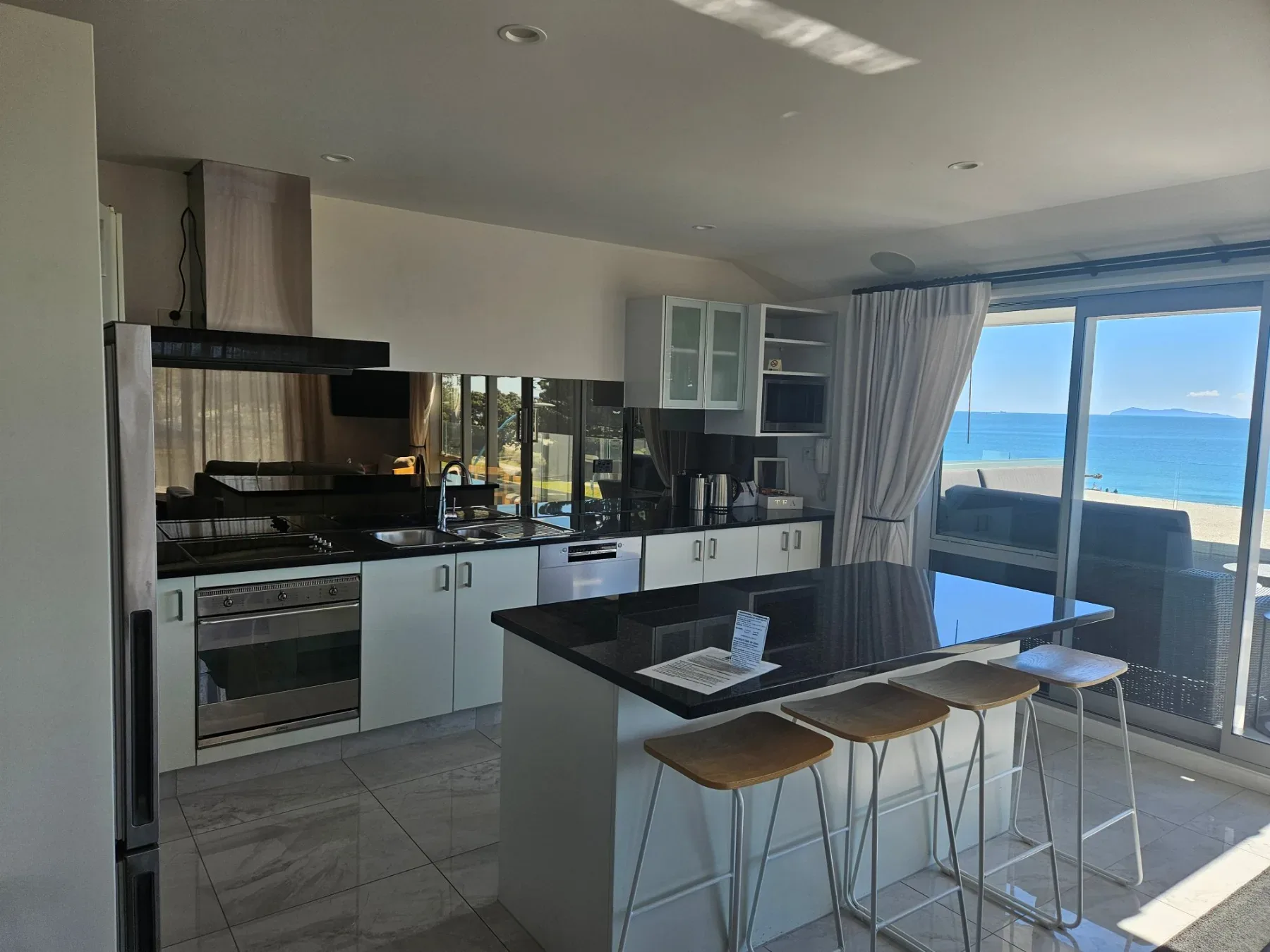 Modern kitchen with black benchtop island, bar stools and ocean views.