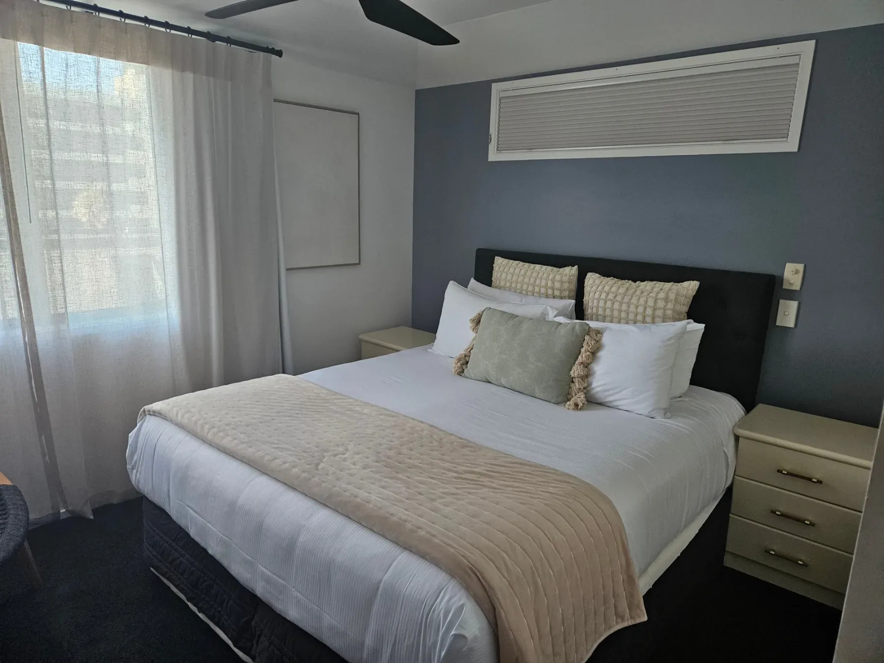 Bedroom with dark upholstered headboard, white bedding and textured cushions.